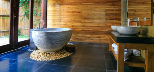 Home builder in NJ uses bamboo for wall in this bathroom with large blue tiles and soaking tup placed on area of pebbles